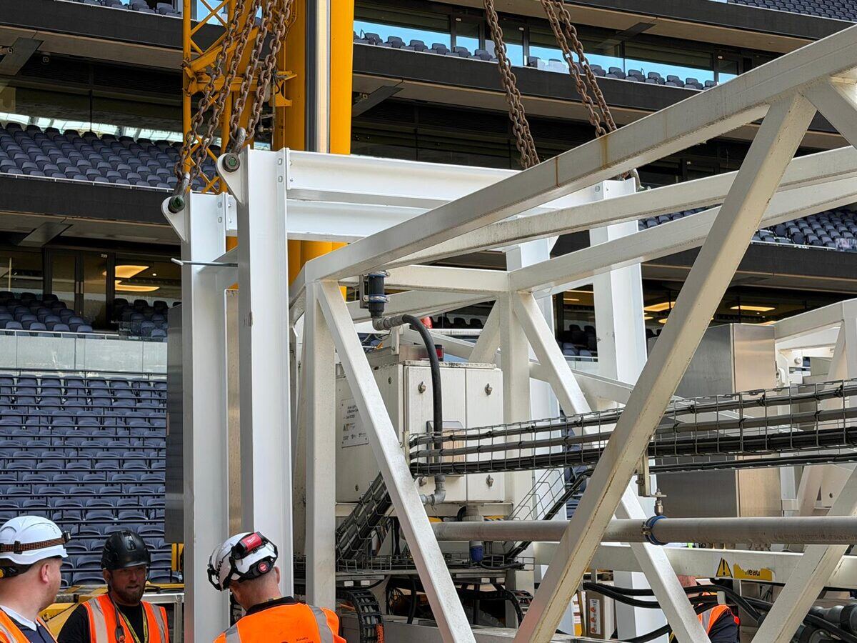 The bespoke LOLER-tested lifting bracket on the pitch with a banksman, the stadium bowl behind